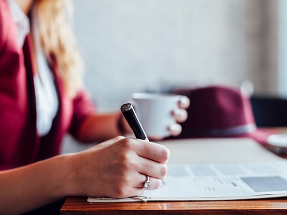 woman writing on a document while having a cup of coffee 